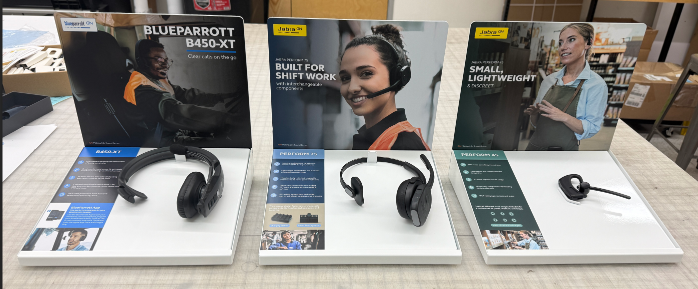 Three finished endcap displays photographed in production, each with a printed panel and a headset mounted in the recessed well below it.